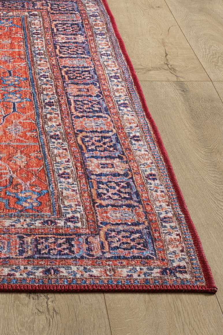 A close-up of the Aurelius Coral Washable Rug - LCC3005 (Custom Size), featuring vibrant red, purple, and blue geometric patterns—ideal for allergy-sensitive homes and high-traffic areas—shown on a light wood floor.