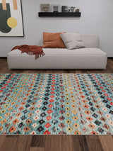 A modern living room with a light gray sofa, two pillows, a rust throw, the Aztec Ambience - Washable Rug - JR1086 (Custom Size) for high-traffic areas, wood floor, abstract wall art, and a black shelf with books and decor.