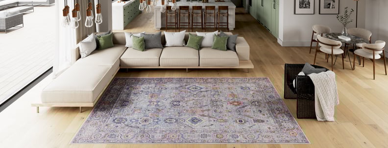 A modern, open-concept living space with a beige sectional sofa, green and gray pillows, the Bellaris Gray Washable Rug - LCC3003 (Outlet) US, a kitchen with barstools, and a dining area with a round table and four chairs.