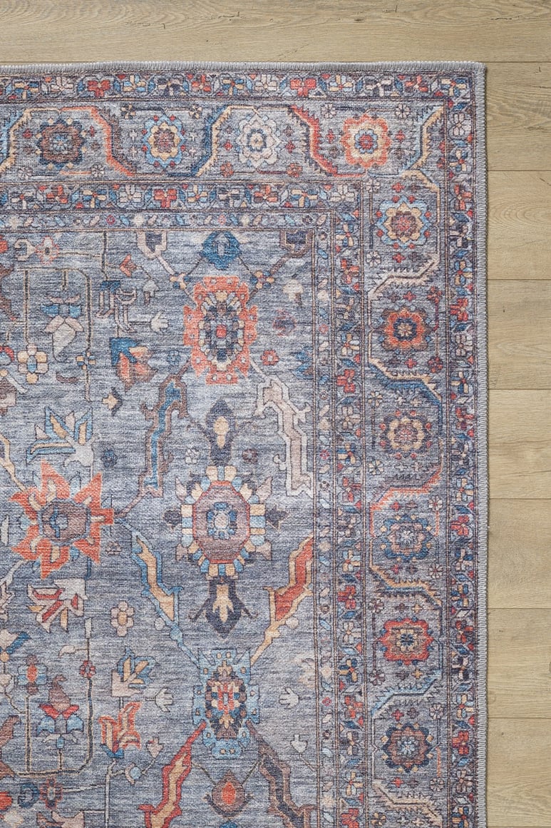 A corner of the Bellaris Gray Washable Rug - LCC3003 (Outlet) US, featuring intricate geometric and floral patterns in blue, gray, red, and orange, is shown laid on light wood flooring.
