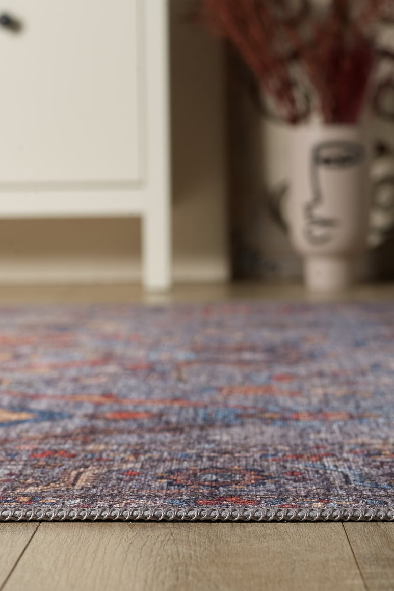 A close-up of the Bellaris Gray Washable Rug - LCC3003 (Outlet) US on a wooden floor, with a white cabinet and a decorative vase with an abstract face design blurred in the background.