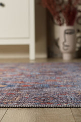 A close-up of the Bellaris Gray Washable Rug - LCC3003 (Outlet) US on a wooden floor, with a white cabinet and a decorative vase with an abstract face design blurred in the background.