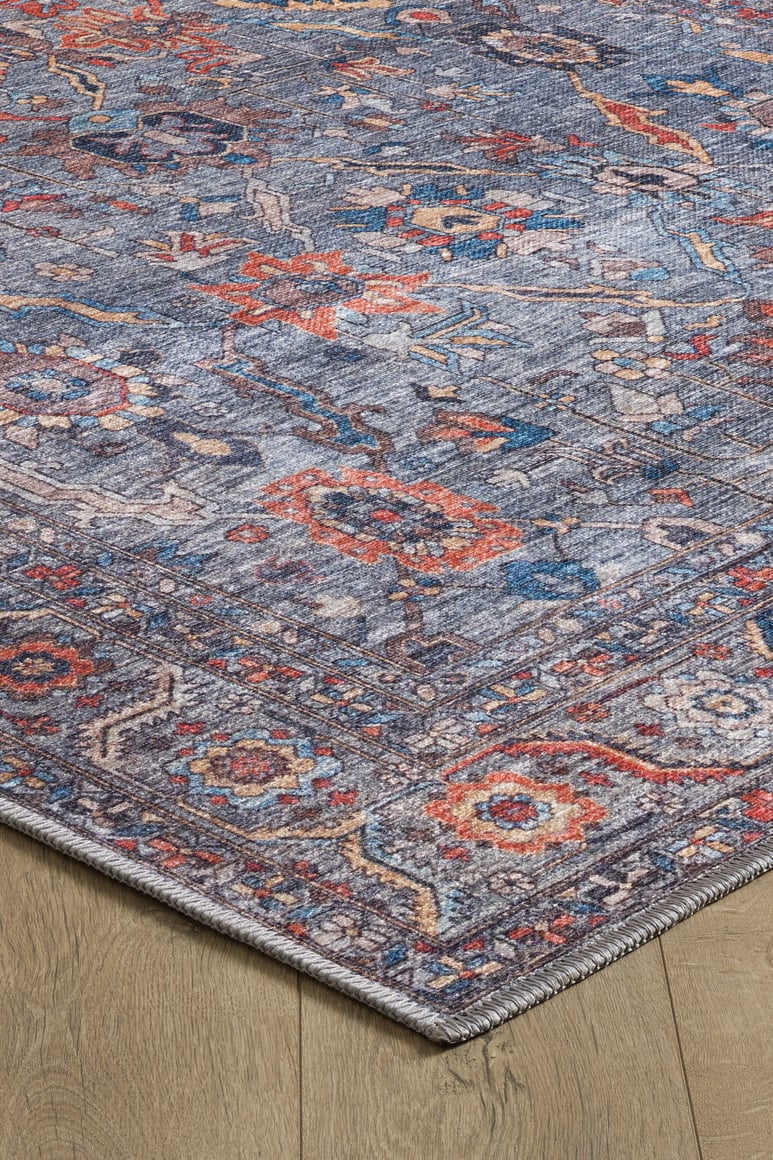 A close-up of the Bellaris Gray Washable Rug - LCC3003 (Custom Size) on a light wooden floor, focusing on one corner to highlight its colorful blue, red, and orange designs, detailed texture, and border.