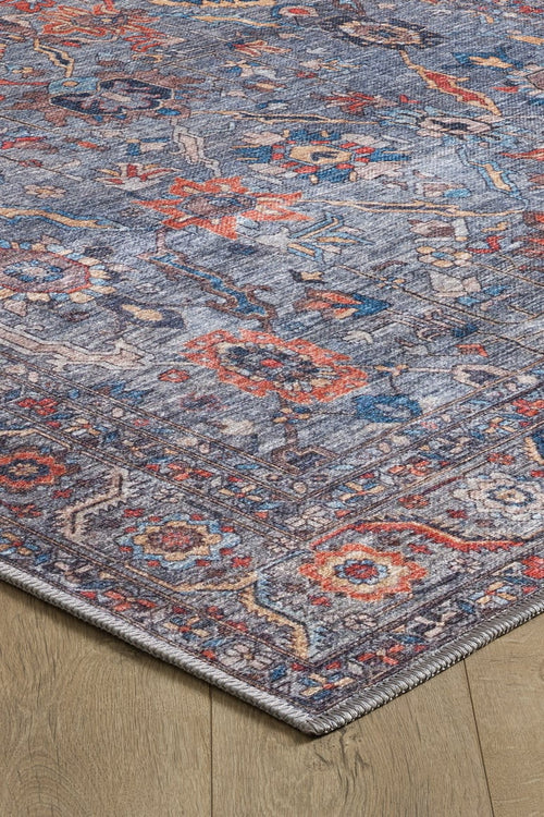 Bild 1 in Galerieansicht laden. A close-up of the Bellaris Gray Washable Rug - LCC3003 (Custom Size) on a light wooden floor, focusing on one corner to highlight its colorful blue, red, and orange designs, detailed texture, and border.