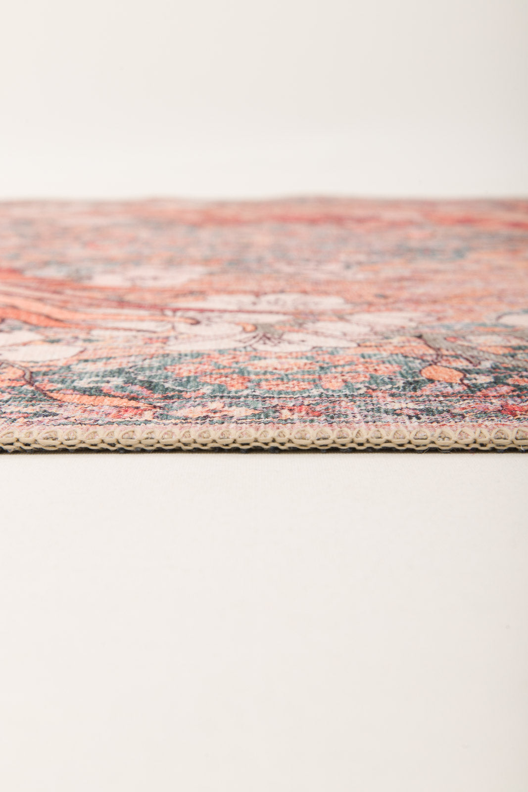 Close-up side view of the Blazefang Myth - Washable Rug (JR0049) featuring a thin, flat weave with a textured edge and vibrant geometric pattern, displayed on a plain light surface against a neutral background.