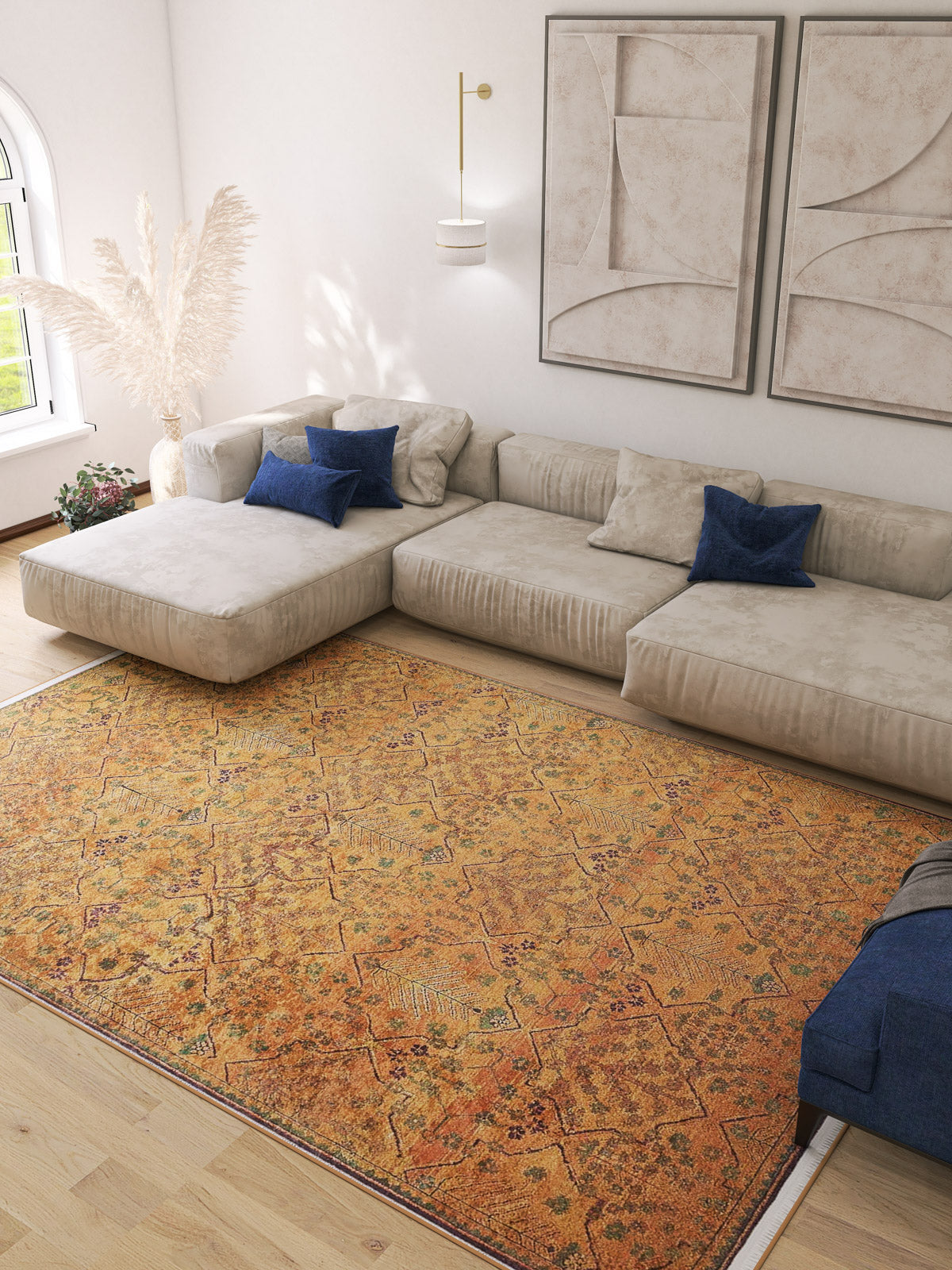 A modern living room with a large beige sectional, blue accent pillows, abstract wall art, and the Blossom Breeze - Washable Rug - JR1752 (Custom Size) in vibrant orange on light wood floors. Sunlight pours in from an arched window.