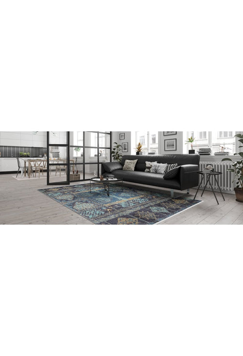 Load image 1 in gallery view. A modern living room features a black sofa, decorative pillows, and the Blossoming Bazaar - Washable Rug - JR1862 in blue—perfect for high-traffic areas. Large windows fill the space with light; plants near the radiator and an open dining area add charm.