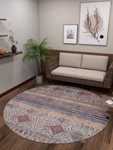 A cozy, modern living room with a light sofa, woven chair, potted plant, wooden floor, and wall art. Floating shelves hold decor on the left wall. A small side table sits next to the vibrant Bohemian Bouquet - Washable Rug - JR5090.