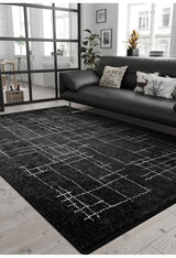 Modern living room with the Bohemian Illusion - Washable Rug - JR1953, black leather sofa with patterned cushions, light wood floor, potted plants, and large windows for natural light. Minimalist decor in monochrome tones.