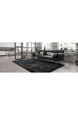 Modern living room featuring a black sofa, patterned cushions, Bohemian Illusion - Washable Rug - JR1953, small round coffee table, potted plants, and wall art, with the dining area and kitchen visible in the background.
