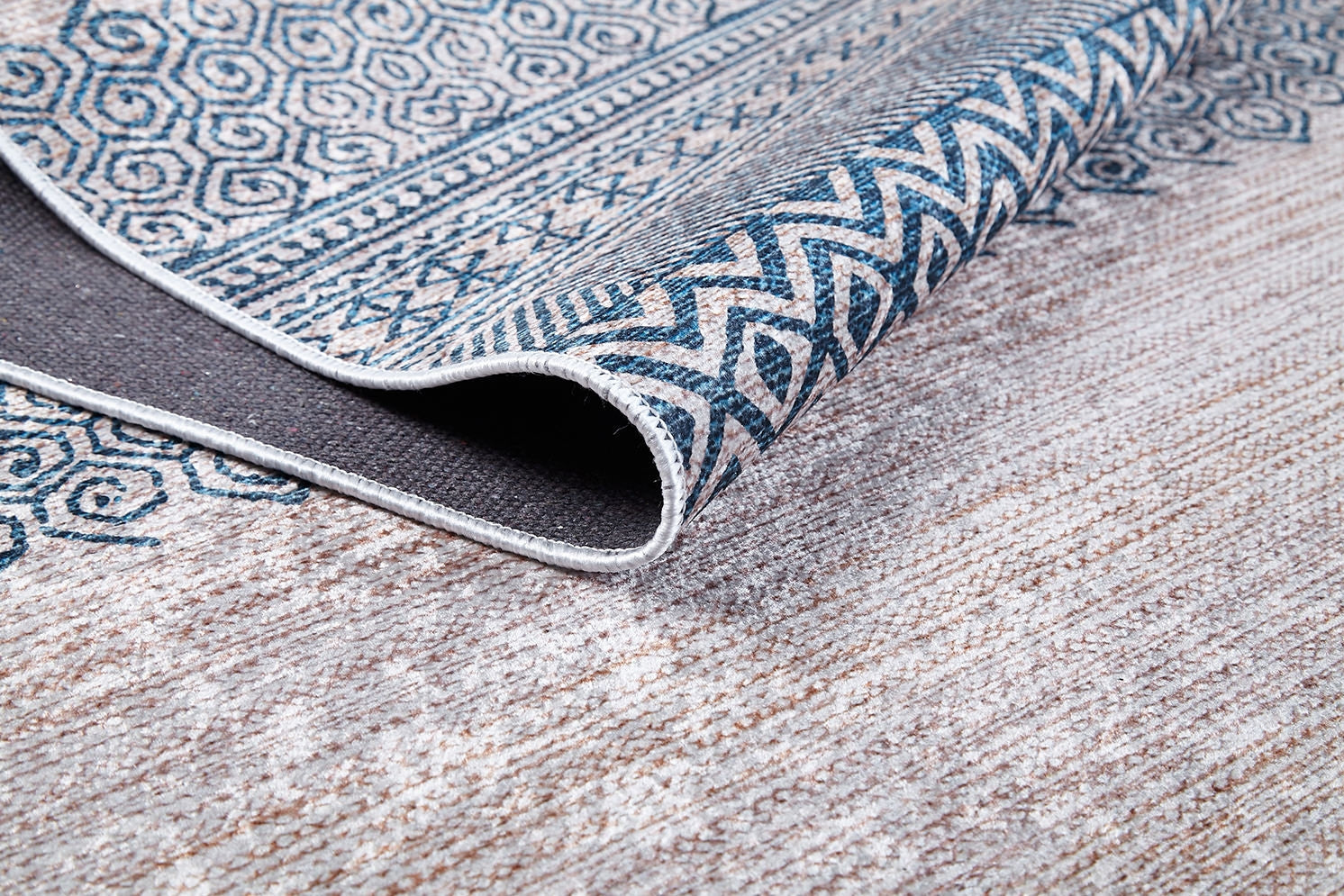 A close-up of the Bohemian Nights - Washable Rug - JR1585, folded to reveal its textured underside. Featuring blue geometric and zigzag designs on a light background, it's perfect for allergy-sensitive homes or high-traffic, neutral-toned floors.