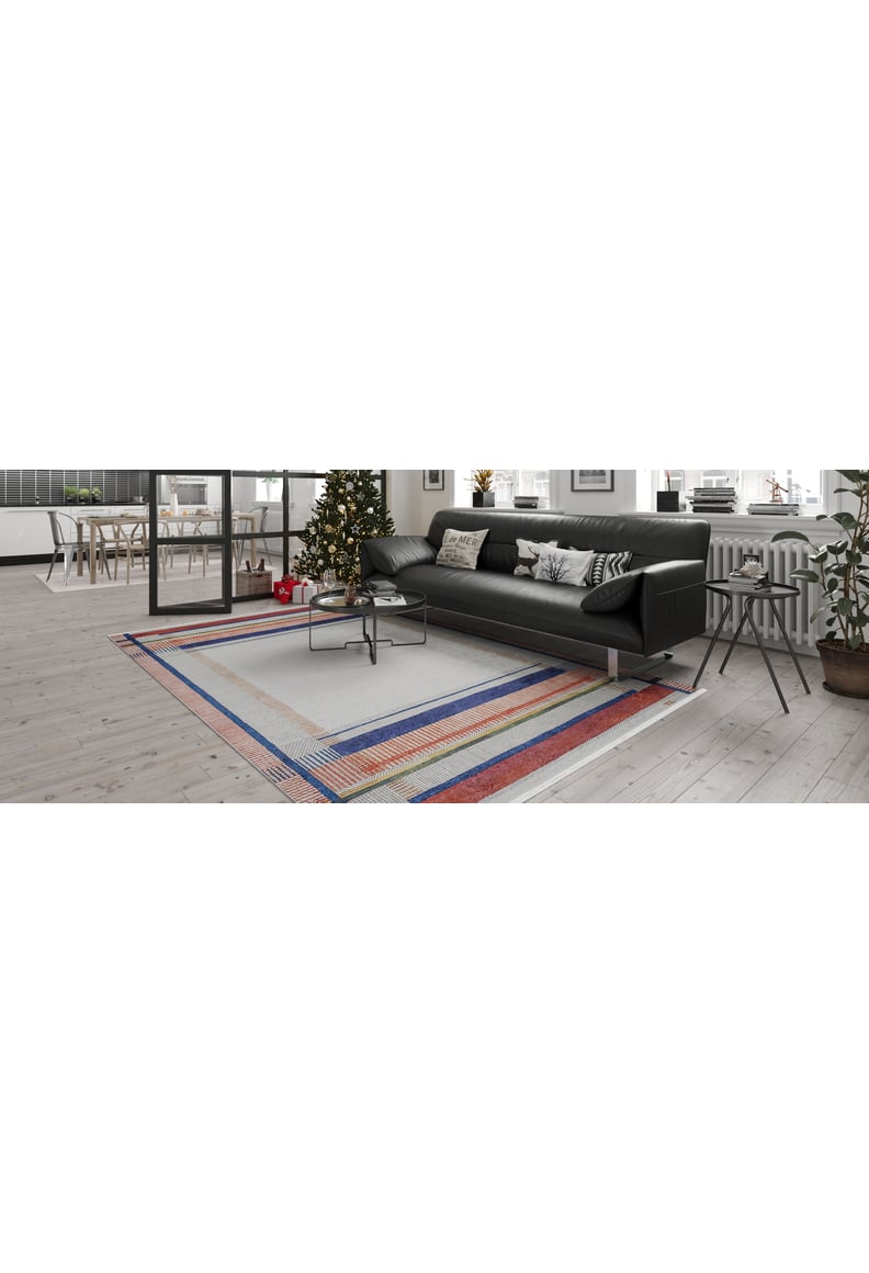 Modern living room featuring a black sectional, Bohemian Nightscape - Washable Rug - JR1701 (Custom Size) ideal for high-traffic areas, coffee table, Christmas tree by the window; dining area with large windows and indoor plants in the background.