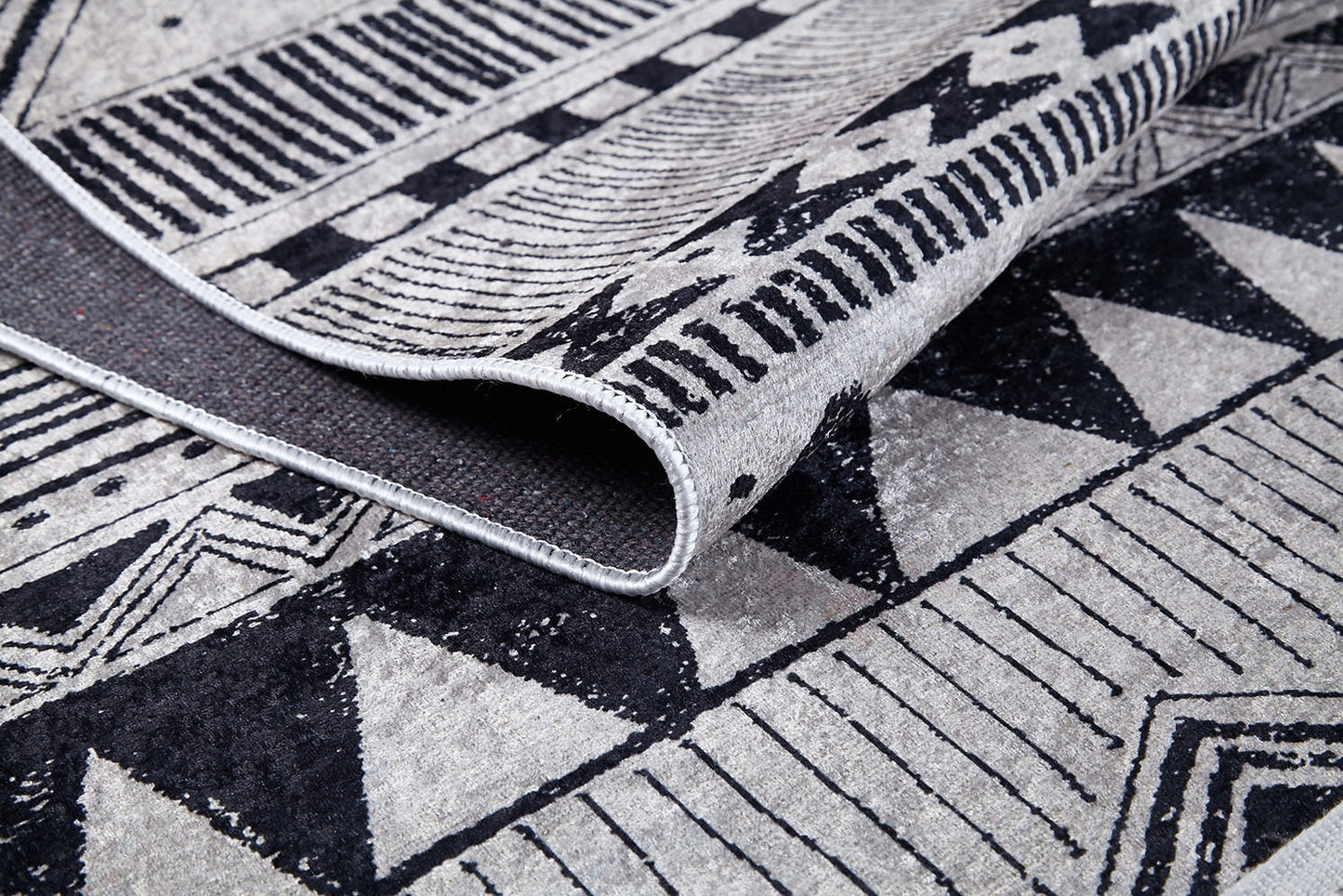 A close-up of Bohemian Sunrise - Washable Rug - JR1713 (Custom Size), folded to show black and gray triangles, stripes, and geometric patterns—ideal as a washable rug for high-traffic areas.