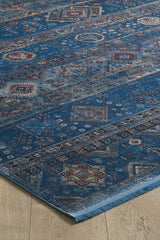 The Bohemian Tracery Rug - Blue - 2221B, featuring intricate geometric and floral patterns in red, beige, and ivory tones, lies on a light wooden floor with a slightly curved corner highlighting its detailed design.