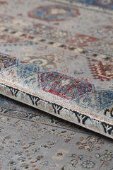 A close-up of the Bohemian Tracery Rug - Grey - 2221C highlights its intricate geometric patterns in blue, red, cream, and beige, showcasing the woven texture and detail with a portion of the rug gently folded.