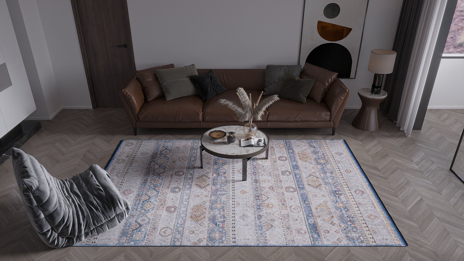 A modern living room features a brown leather sofa, cushions, a round marble coffee table, a vase with dried grass, and the Bohemian Tracery Rug - Grey - 2221C in geometric patterns. Contemporary art hangs over a gray accent chair.