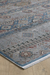 A close-up of the Bohemian Tracery Rug - Grey - 2221C, featuring blue, red, and beige traditional geometric patterns on a light background. The rug lies on a wooden floor with one corner displaying its fringed edges.