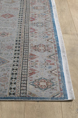 A close-up of the Bohemian Tracery Rug - Grey - 2221C shows geometric and floral patterns in blue, red, and beige on a light wood floor. This rectangular machine-made rug features a detailed border and fringed edges.
