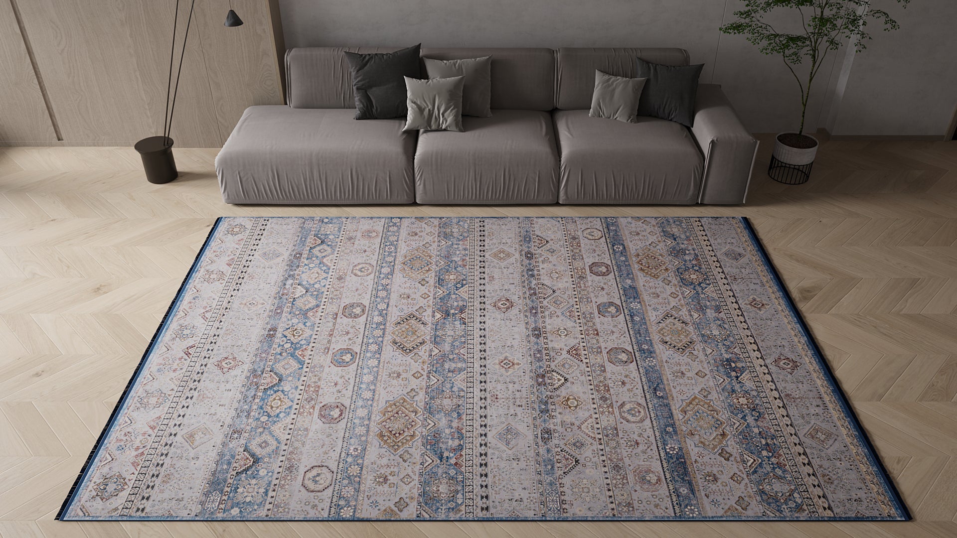 A modern living room with a beige sofa, assorted cushions, potted plant, floor lamp, and the Bohemian Tracery Rug - Grey - 2221C, featuring blue and beige geometric patterns on a light wood floor.
