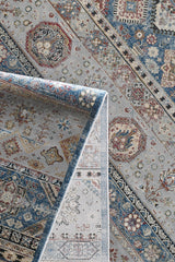 A detailed view of the Bohemian Tracery Rug - Grey - 2221C, a blue and grey machine-made rug with intricate floral and geometric patterns in red, cream, and beige, shown partly folded to display both sides.