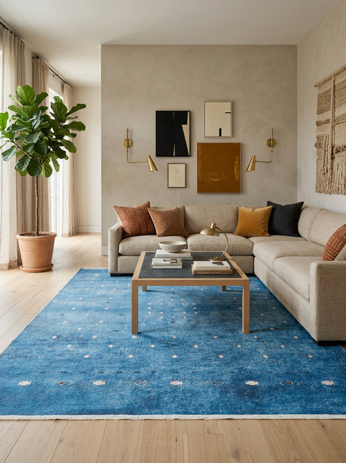 Load image 1 in gallery view. A modern living room with a beige sectional sofa, brown and orange cushions, the Bohemian Whirlwind - Washable Rug - JR1989 perfect for high-traffic areas, a wooden coffee table with books, wall art, gold sconces, a potted plant, and light wood floors.