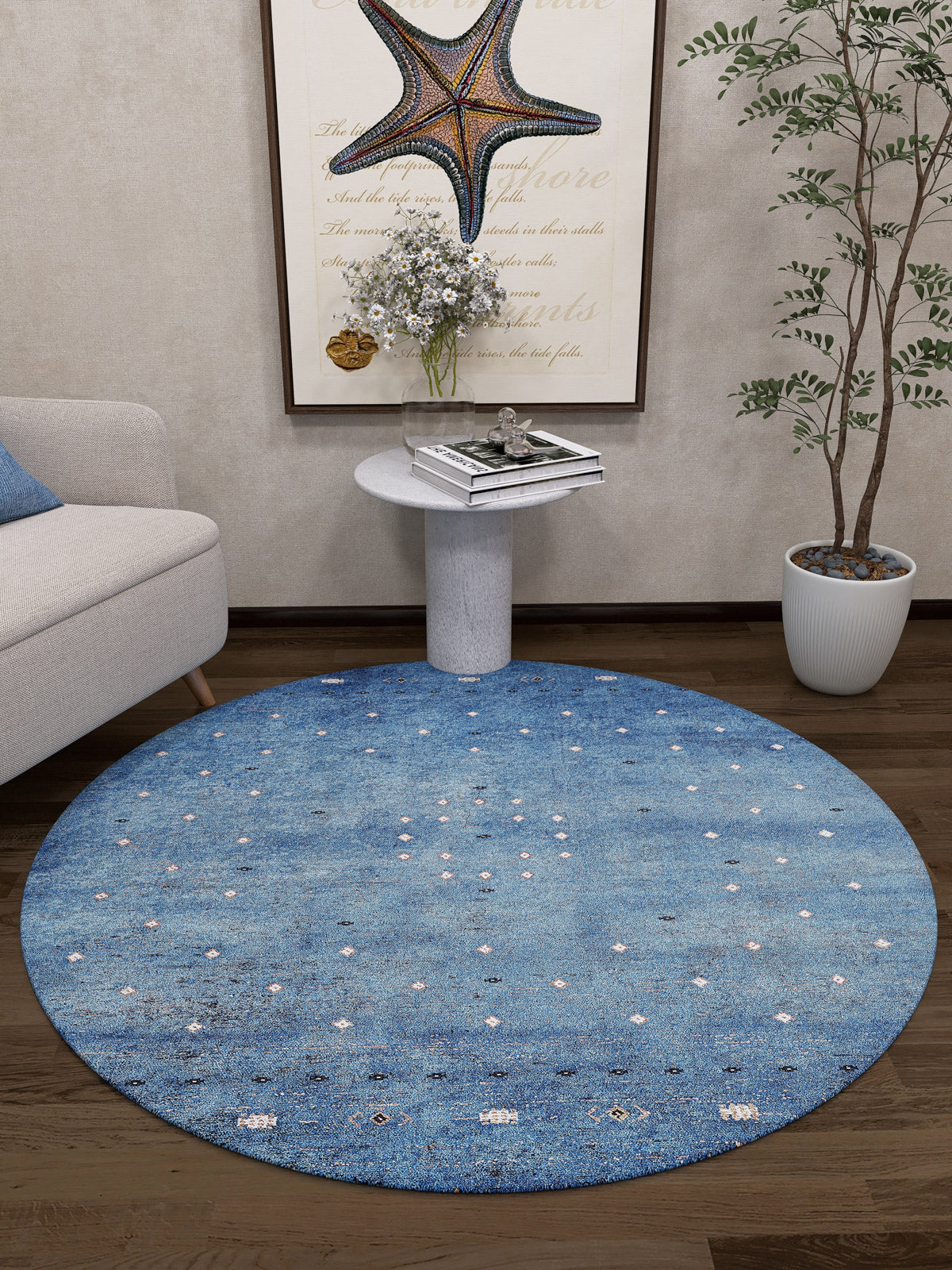 A cozy living room corner with the Bohemian Whirlwind - Washable Rug - JR1989, ideal for high-traffic areas, a marble side table with flowers and books, framed starfish art, a beige sofa, a tall potted plant, and dark wooden floors.