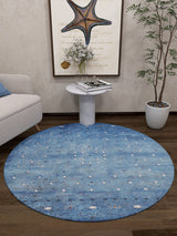 A cozy living room corner with the Bohemian Whirlwind - Washable Rug - JR1989, ideal for high-traffic areas, a marble side table with flowers and books, framed starfish art, a beige sofa, a tall potted plant, and dark wooden floors.