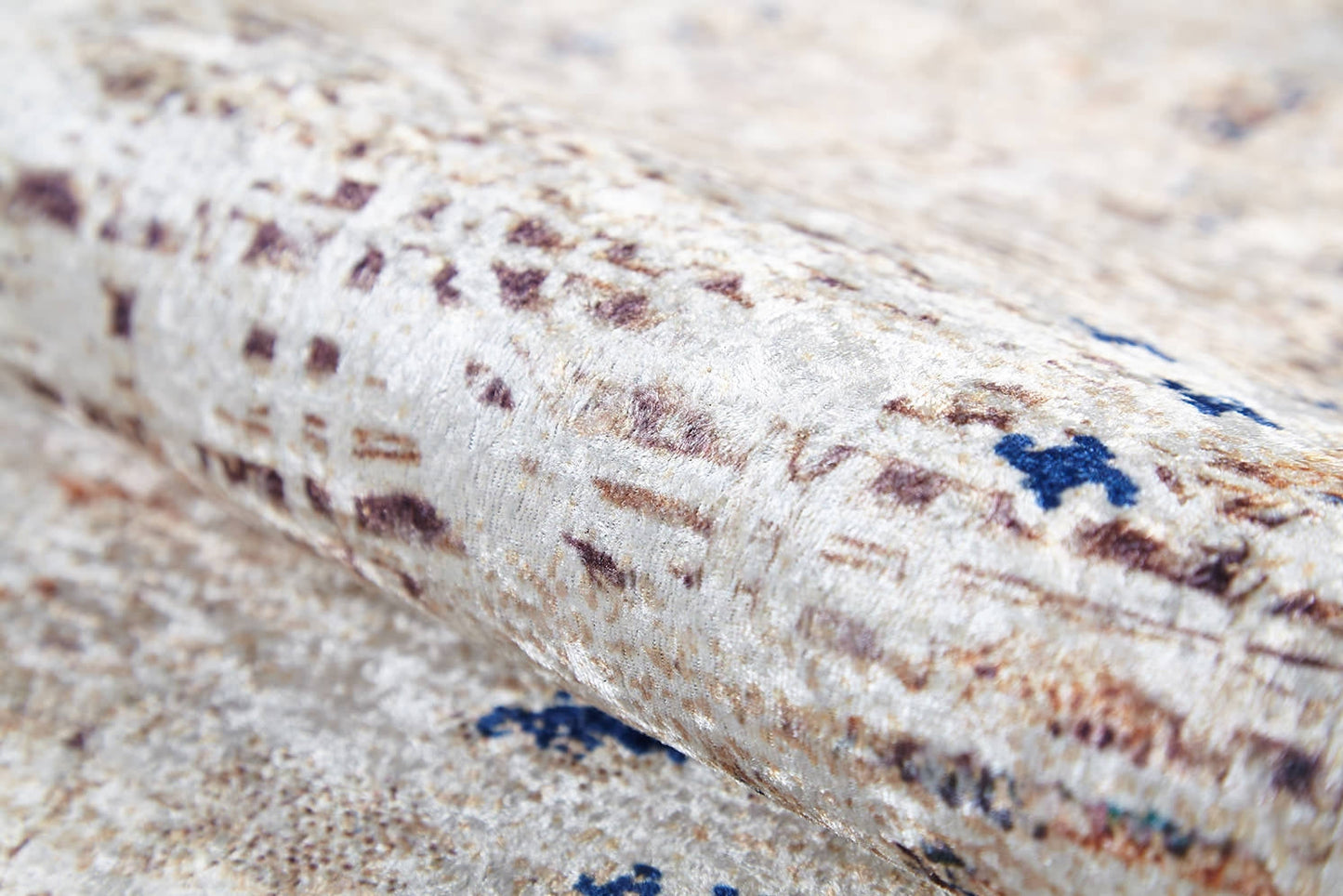 A close-up of the Boho Babe - Washable Rug - JR1664 (Custom Size) shows its textured, rolled surface and beige, brown, and blue abstract pattern. The soft, slightly shiny fabric is perfect for high-traffic areas and showcases subtle color variations.