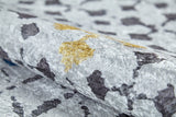 A close-up of the Boho Breeze - Machine-Washable Rug - JR5011 (Custom Size) shows silver velvet fabric with a textured surface and abstract dark gray and gold patches, evoking a luxurious look ideal for high-traffic areas.