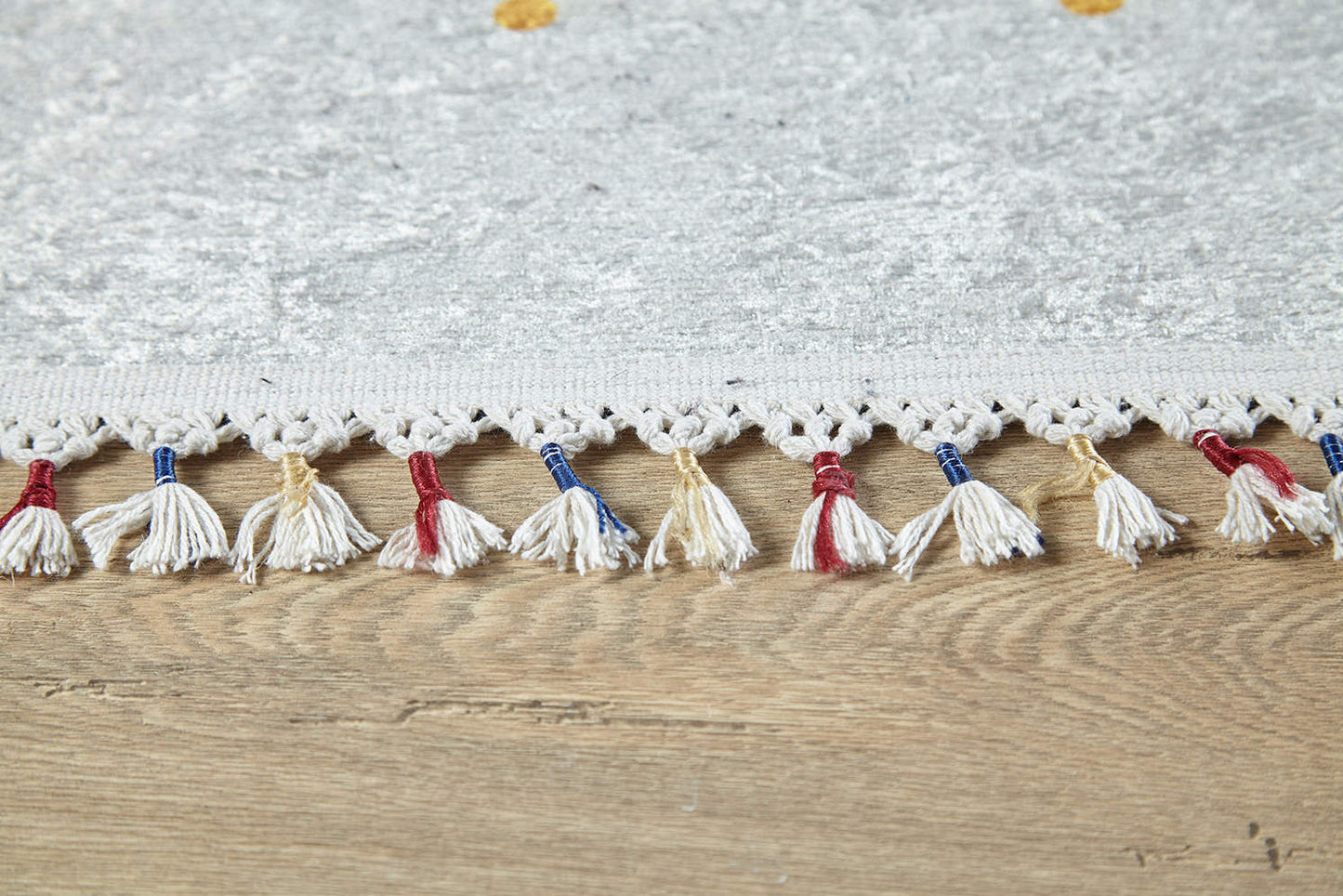 Close-up of the Boho Chic - Washable Rug - JR5103 (Custom Size), a light gray flat weave with decorative tassels and red, blue, and beige threads—ideal for high-traffic areas and shown on a wooden floor.