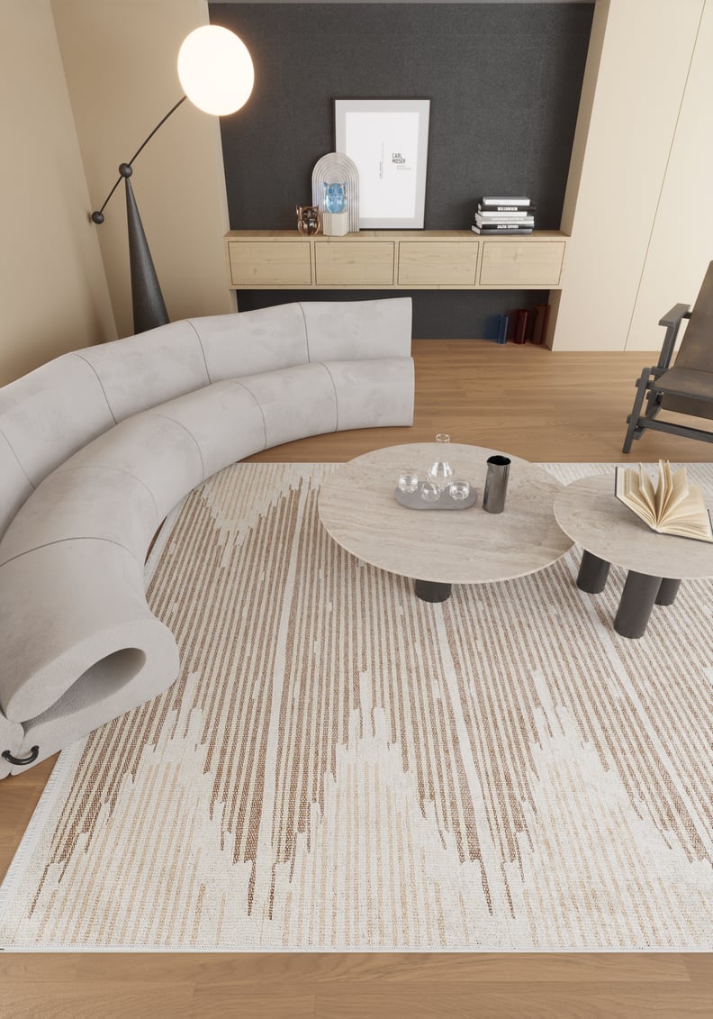 Modern living room with a curved light-gray sofa, Boho Paradise - Washable Rug - JR2004 in cream and beige, two round coffee tables with books and glassware, wooden floor, floor lamp, and a console with decor against a dark accent wall.