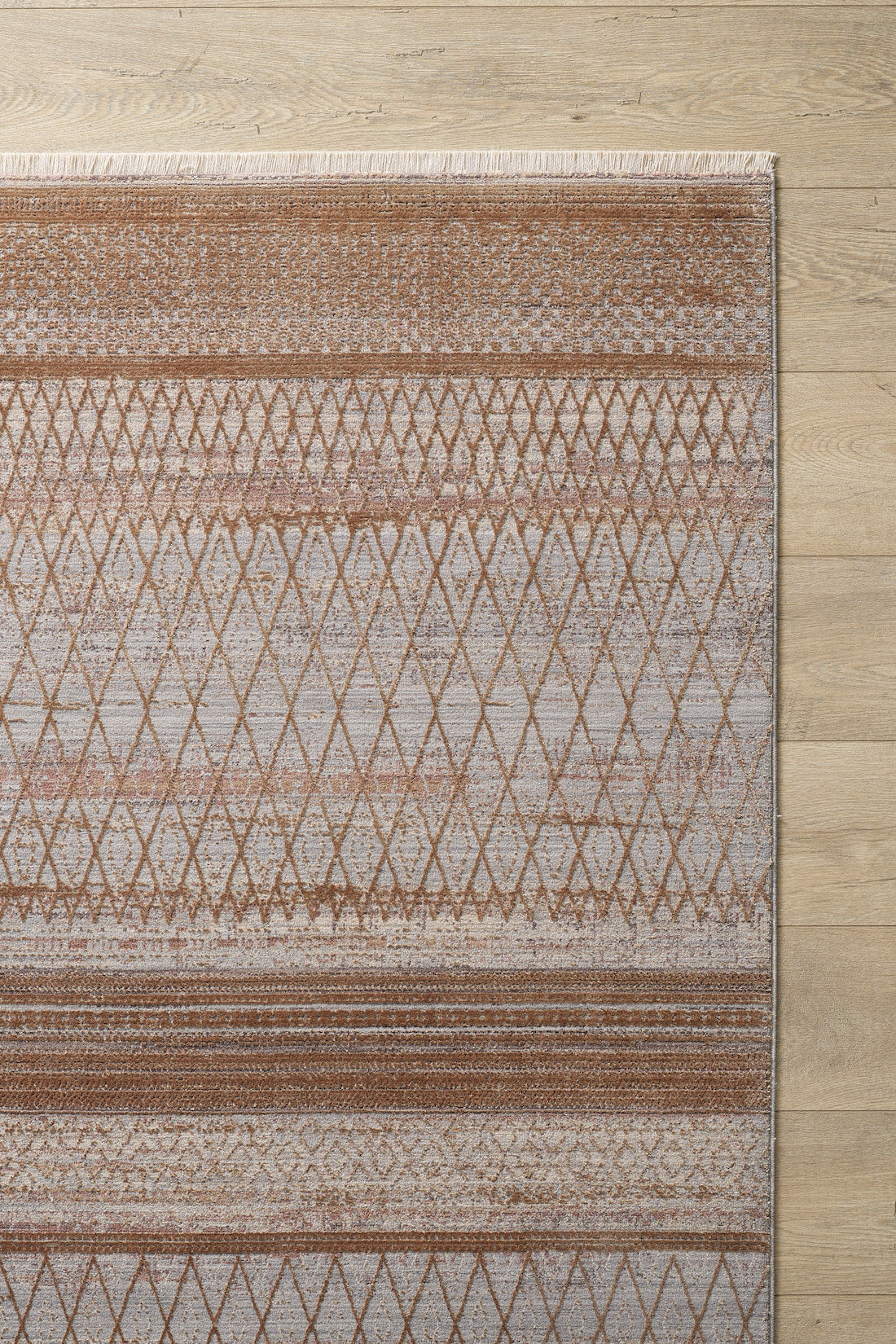 The Boho Sunset Trellis Rug - HRD004 is a machine-made area rug with diamond and stripe patterns in brown and beige, set on a light wood floor. It features a stylish fringed edge on one side for added flair.