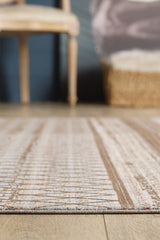 A close-up of the Boho Sunset Trellis Rug - HRD004 in light brown and cream on a wooden floor, with a wooden chair and woven basket softly blurred in the background.