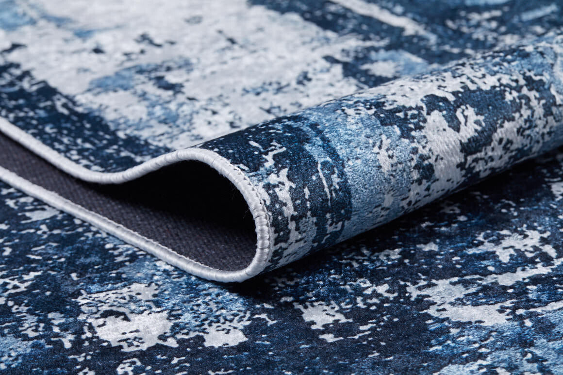 A close-up of the Bold Blooms - Washable Rug - JR836 (Custom Size) in blue with white abstract patterns, showing a folded edge and detailed border stitching—ideal for high-traffic areas and easy to clean.