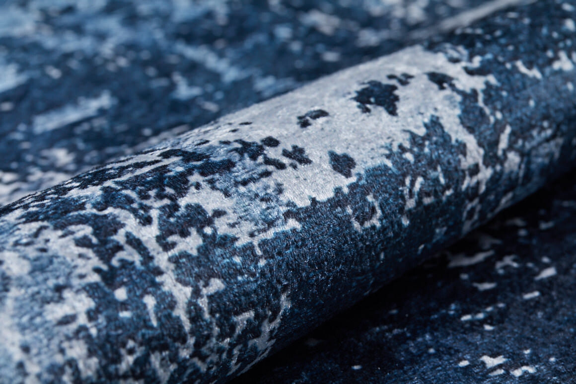 A close-up of the Bold Blooms - Washable Rug - JR836 (Custom Size), featuring a rolled-up blue design with textured, abstract patterns in blue, white, and black—resembling watercolor and perfect for high-traffic areas. Easy to maintain and washable.