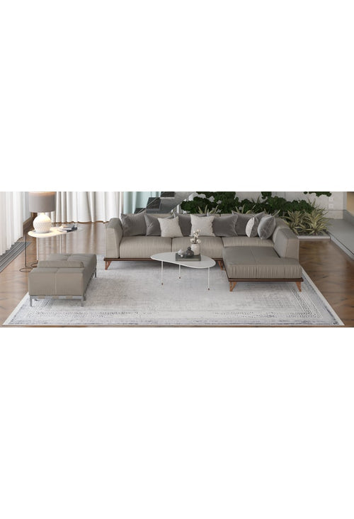 Load image 1 in gallery view. A modern living room features a gray sectional, ottoman, white oval coffee table, décor items, and the Bold Borderline - Washable Rug - JR1984—ideal for high-traffic areas. Green plants and sheer curtains brighten the space.