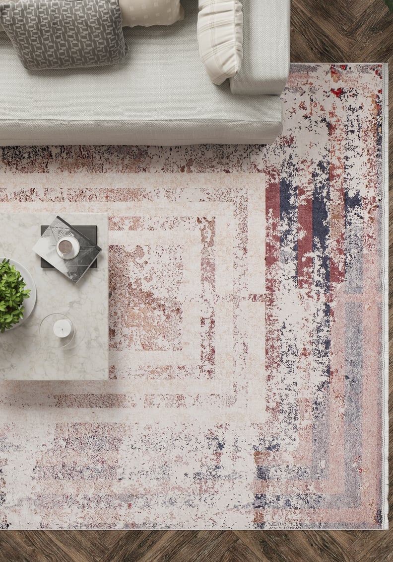 A modern living room with a light gray sofa, white and patterned cushions, a white marble coffee table with a plant, and the Bold and Geometric - Washable Rug - JR1410 in cream, red, and blue—perfect for high-traffic areas—on dark wood floors.