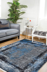 A living room with the Bold and Minimalist - Washable Rug - JR1229 (Custom Size) in blue, a gray sofa with pillows, white chair with blanket, small side table with flowers, and a tall green plant on a high-traffic wooden floor.