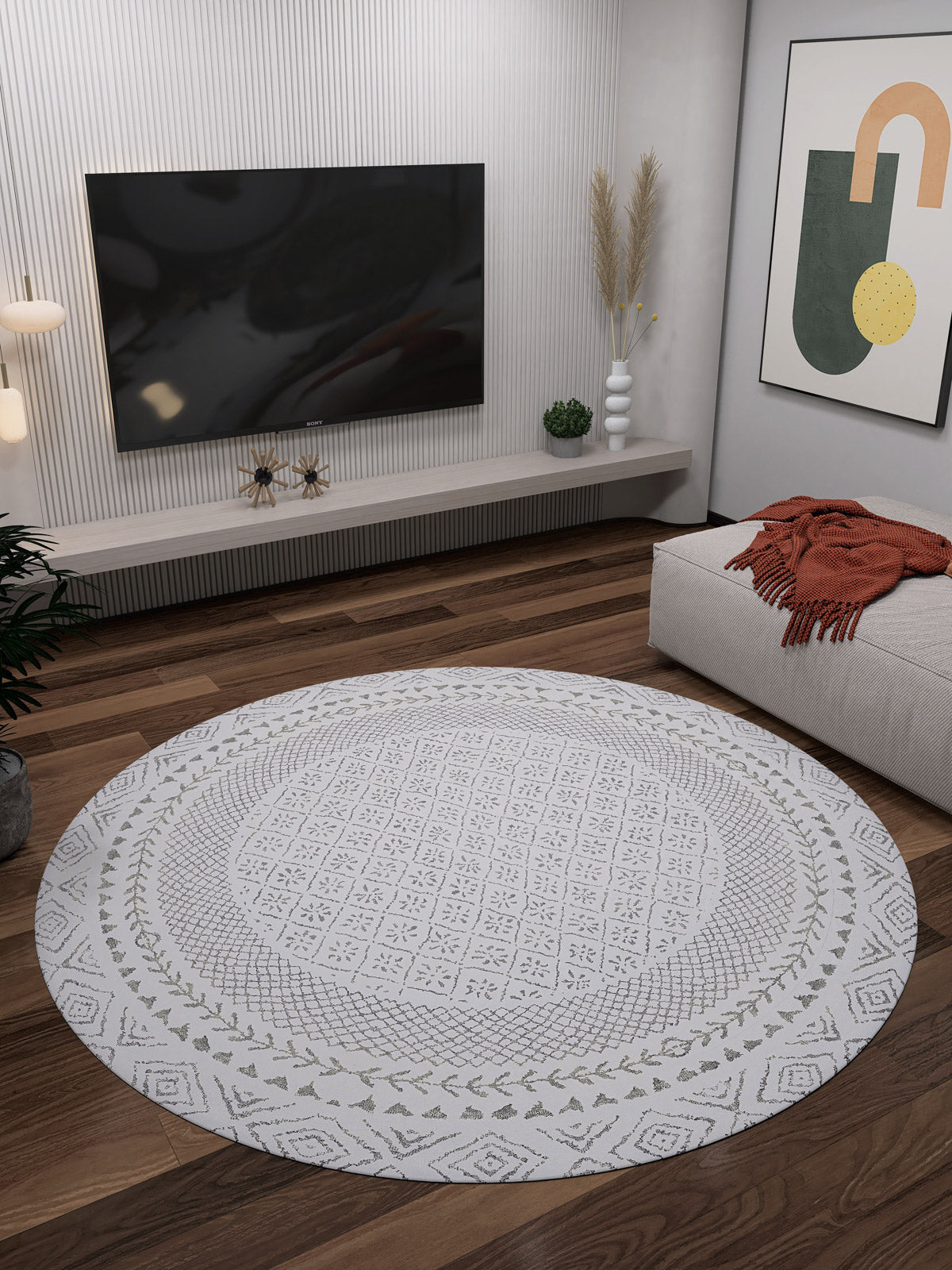 A modern living room features the Borderline Brilliance - Washable Rug - JR1987 with bold patterns on a wooden floor, a wall-mounted TV, abstract artwork, a gray sofa with an orange throw, and decorative plants on a minimalist shelf.