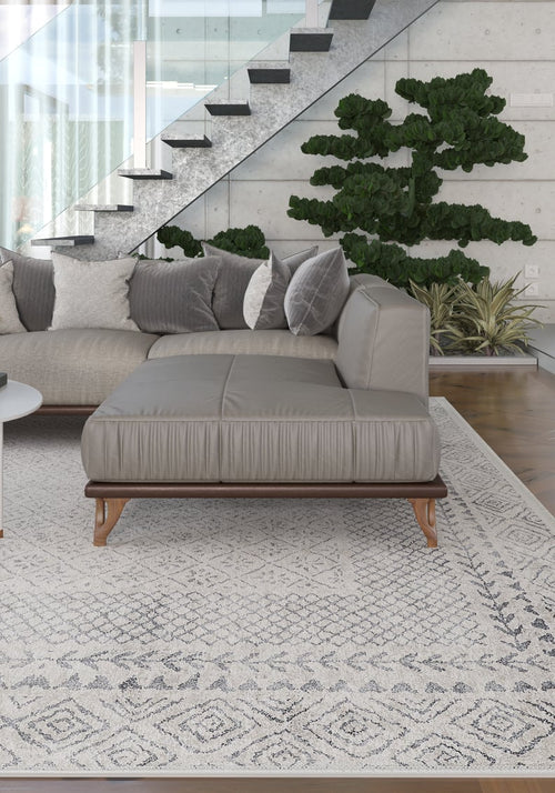 Load image 1 in gallery view. Modern living room with a gray sectional sofa, the Borderline Brilliance - Washable Rug - JR1987, large green plant, and glass-railed staircase. Neutral tones and minimalist decor provide a calm, contemporary vibe for busy spaces.
