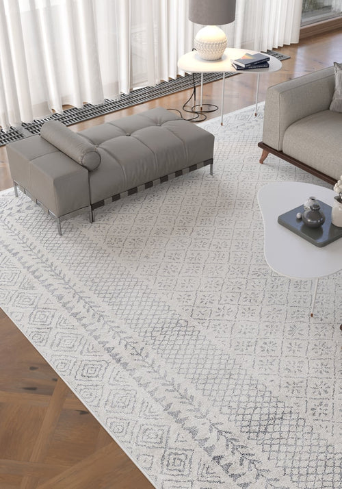 Bild 1 in Galerieansicht laden. Modern living room with the Borderline Brilliance - Washable Rug - JR1987 (Custom Size), a gray bench and sofa, white coffee table with decor, round side table with lamp, and large windows—ideal for high-traffic areas.