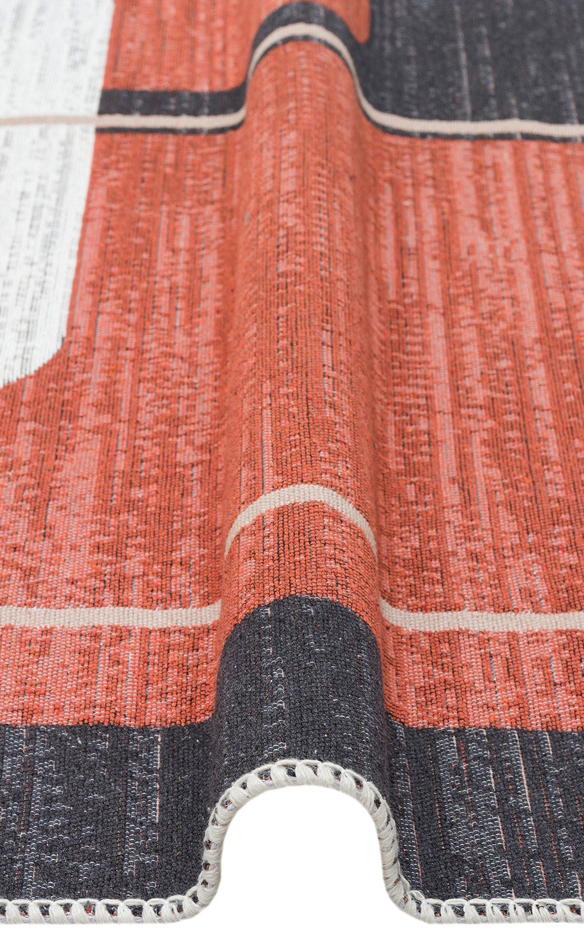 A close-up of the Burnt Stone - Washable Reversible Kilims - AR36 shows its modern geometric red, black, and white design, with the edge gently lifted and detailed border stitching.