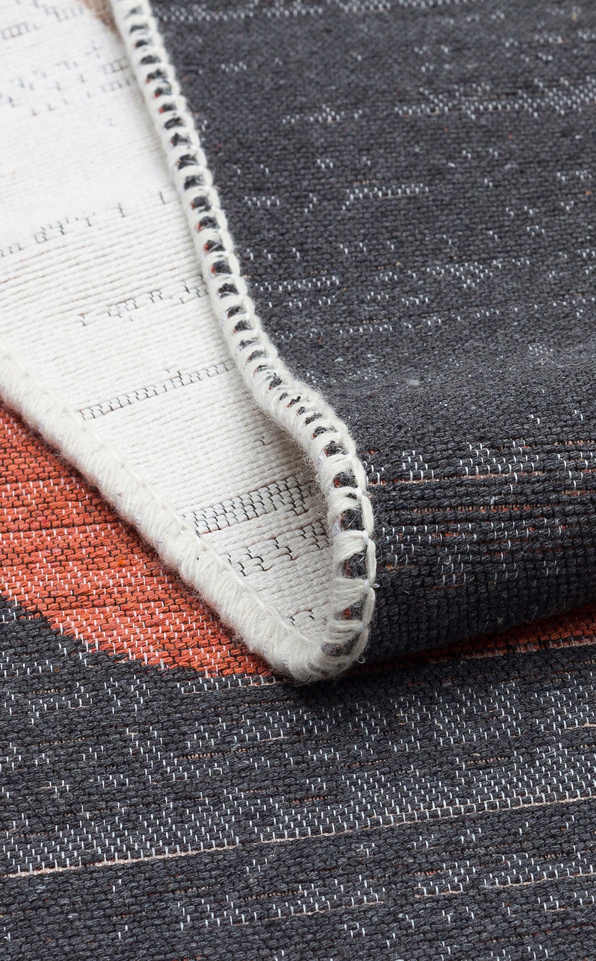 A close-up of the Burnt Stone - Washable Reversible Kilims - AR36 shows textured gray, white, and orange threads with a folded corner, a stitched white edge, and intricate weaving details on both sides.