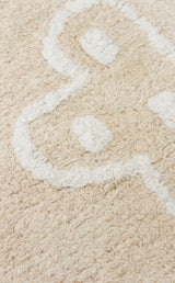 A close-up of the Calm Nest - Washable Shaggy - CBN16 rug in cream beige, featuring ultra-soft, fluffy fibers and a white abstract curved pattern.