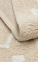 A close-up of the Calm Nest - Washable Shaggy - CBN16 rug in cream beige shows white patterns and a softly folded corner exposing its woven underside.