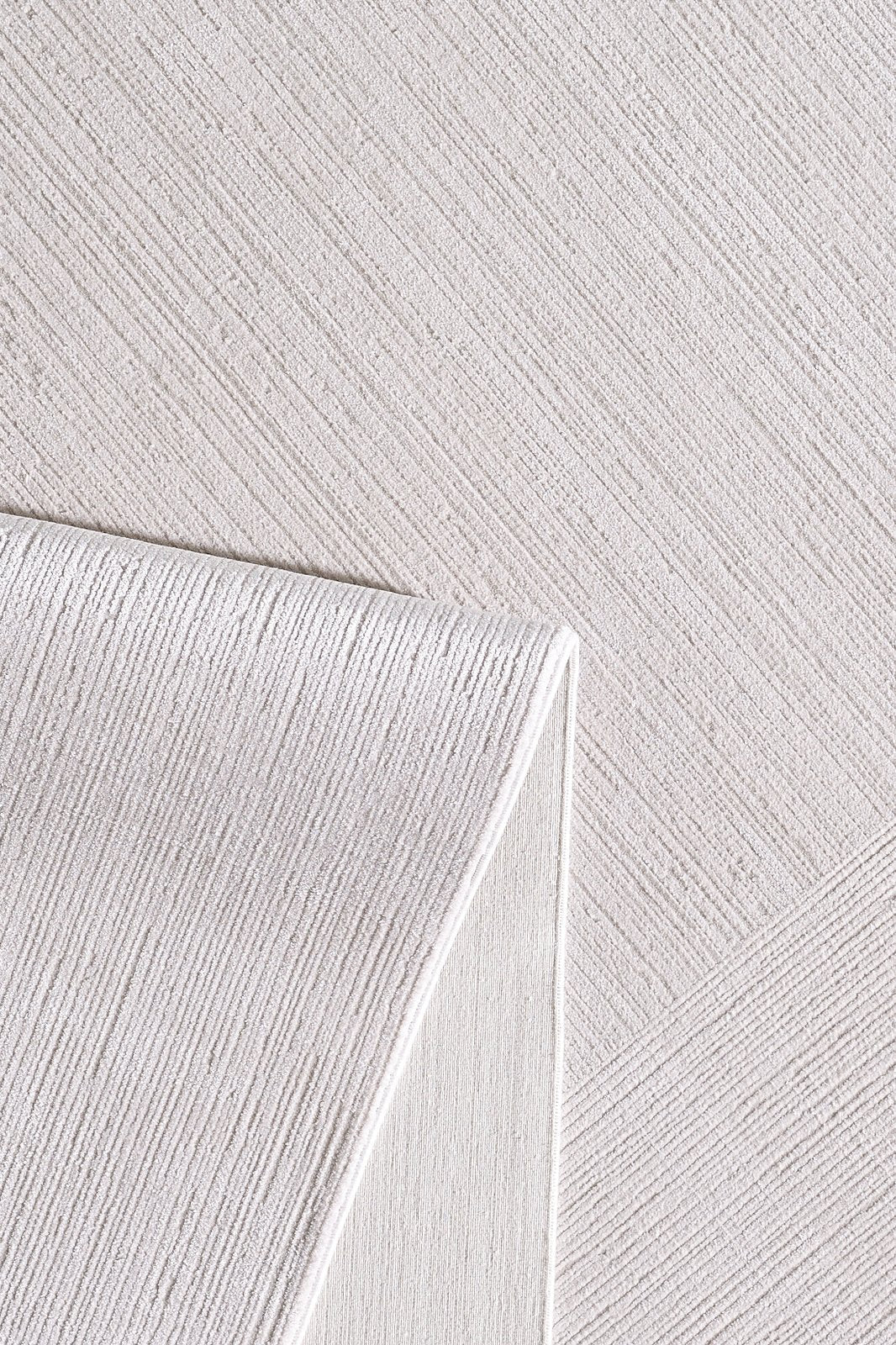 A close-up of the Candlelight Comfort Modern Ivory Rug - EW2824 shows its textured, off-white fabric with diagonal stitched lines and a folded corner that reveals both sides of this luxury machine-made area rug.