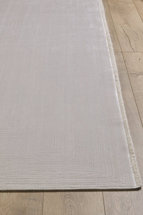 Load image 1 in gallery view. A close-up of the Candlelight Comfort Modern Ivory Rug - EW2824, a machine-made, neutral-toned rug with subtle textured lines and short fringe on one edge, shown atop a warm wooden floor for a soft look.