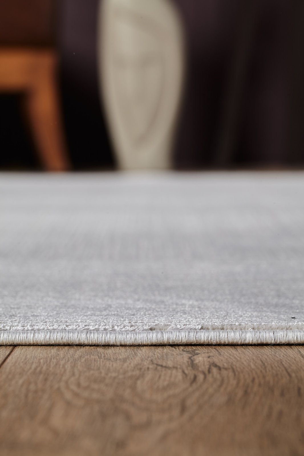 Close-up of the edge of the Candlelight Comfort Modern Ivory Rug - EW2824 on a wooden floor, with blurred furniture and decor in the background.