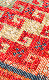 Close-up of the Canyon Shade - Kilim - NMD11 rug, showcasing its woven red base with geometric patterns in cream, blue, and orange. Squares and lines create a textured, handcrafted look—ideal for modern interiors.