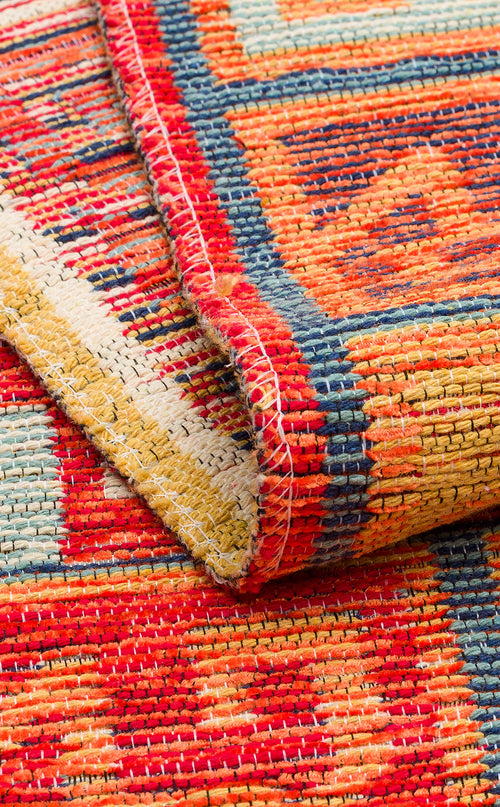 Bild 1 in Galerieansicht laden. Close-up of the Canyon Shade - Washable Reversible Kilim (NMD11), featuring bold red, yellow, blue, and orange geometric tribal patterns. A folded corner reveals detailed stitching and texture on this vibrant washable rug.
